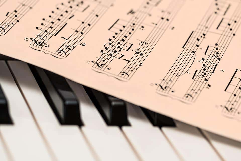 Ein Blatt mit gedruckten Musiknoten liegt auf den schwarzen und weißen Tasten eines Klaviers.