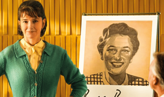 Eine Frau in einer grünen Strickjacke steht neben einer Staffelei mit dem großen Porträt einer anderen Frau an einer gelb getäfelten Wand.
